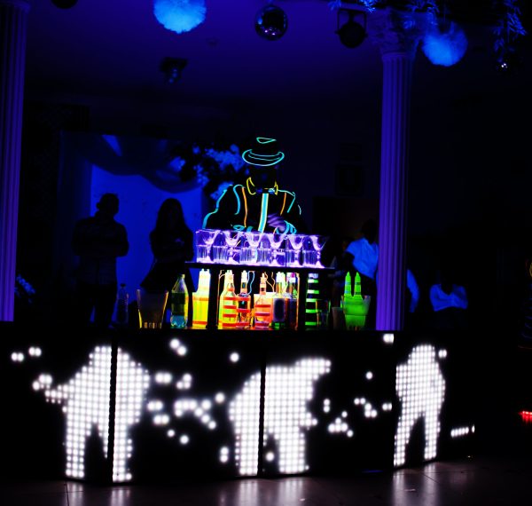 Professional barman and led light show. Silhouette of modern bartender shaking drink at night cocktail bar.